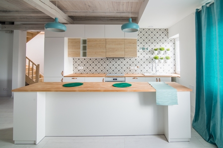 Open bright kitchen with white furniture. Island kitchen. Turquoise lamps and curtains. Modern, bright attic apartment.の写真素材