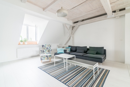 Bright attic living room with wooden ceiling beams. Grey fabric sofa. Modern, bright attic apartment.の写真素材