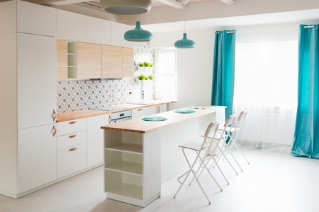 Modern white kitchen cabinets with Induction hob. Open bright kitchen with white furniture. Island kitchen. Turquoise lamps and curtains. Modern, bright attic apartment.の写真素材