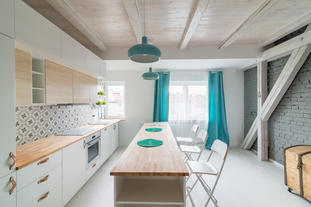 Modern white kitchen cabinets with Induction hob. Open bright kitchen with white furniture. Island kitchen. Turquoise lamps and curtains. Modern, bright attic apartment.の写真素材