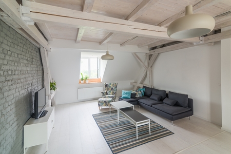 Bright modern living room with television set and fabric couch. Grey brick wall and wooden ceiling beams. Modern, bright attic apartment.の写真素材