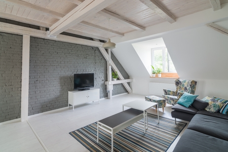 Bright modern living room with television set and fabric couch. Grey brick wall and wooden ceiling beams. Modern, bright attic apartment.の写真素材