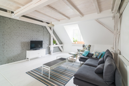 Bright modern living room with television set and fabric couch. Grey brick wall and wooden ceiling beams. Modern, bright attic apartment.の写真素材