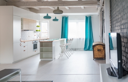 Loft kitchen with white furniture. Island kitchen. Turquoise lamps and curtains. Modern, bright attic apartment.の写真素材