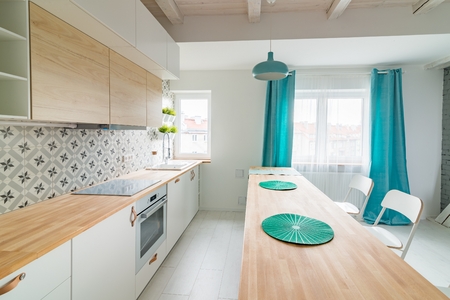 Open bright kitchen with white furniture. Island kitchen. Turquoise lamps and curtains. Modern, bright attic apartment.の写真素材