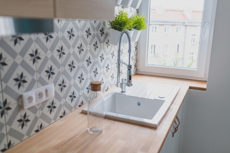 White kitchen sink with chrome faucet. Open bright kitchen with white furniture.の写真素材