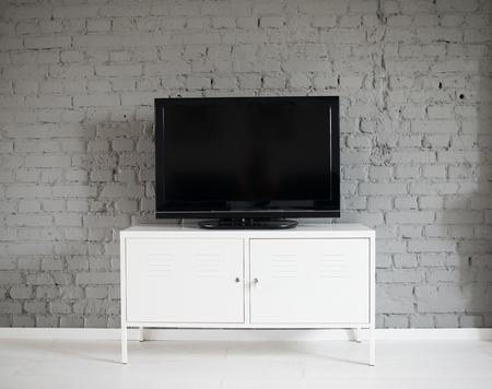 Modern flat lcd television set on white cabinet. Grey brick wall. Modern, bright attic apartment.の写真素材