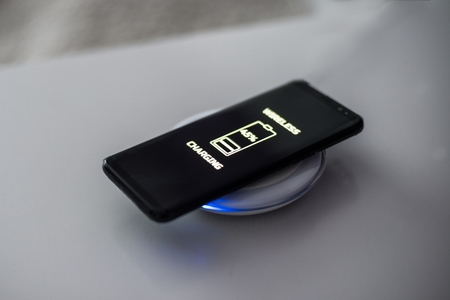 Black touchscreen smartphone wireless charging on induction charger. Wireless chargerの写真素材
