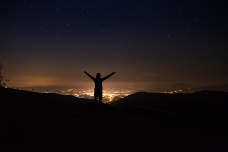 Young woman standing at mountain top at night and looking on city lights. Polish Silesian Beskid, Szczyrk, Polandの写真素材
