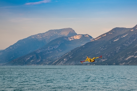 Firefighter water bomber refilling water in Garda Lake. Burning forest in Italian mountains in Brescia province. Forest fire and firefighter planeのeditorial素材