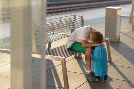 Sad alone boy child waiting alone with his baggage on train station stationの写真素材