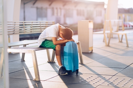 Sad alone boy child waiting alone with his baggage on train station stationの写真素材