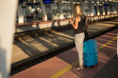 Woman waiting for train on train station platform and checking online scheduleの写真素材