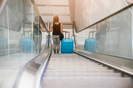 Back view of beauty woman traveling and holding her baggage on escalator on airport or train stationの写真素材