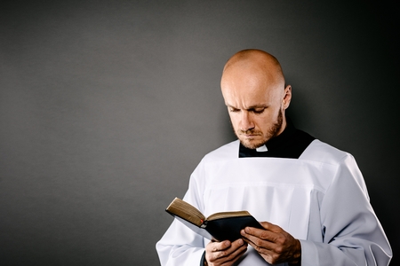 Catholic priest in white surplice reading bible and prayingの写真素材