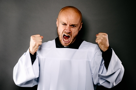 Shouting upset catholic priest in white surplice and black shirt with white collarの写真素材