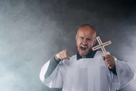Catholic priest exorcist in white surplice and black shirt with cleric collar praying with crucifixの写真素材