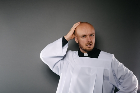 Confused catholic priest in white surplice and black shirt with cleric collarの写真素材
