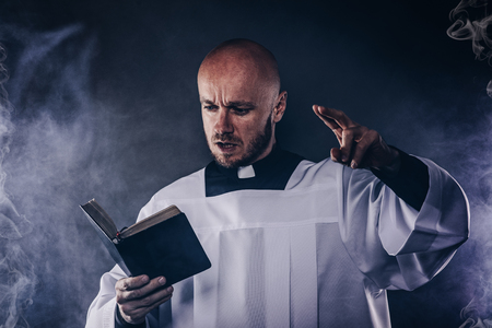 Catholic priest in white surplice and black shirt with cleric collar reading bible and preaching a sermonの写真素材