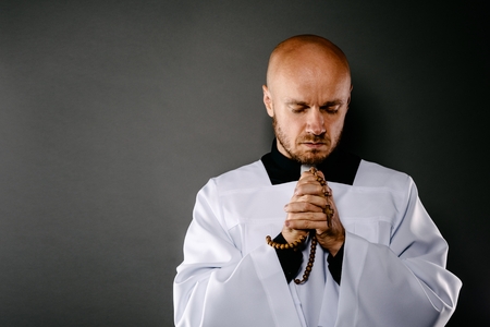 Catholic priest in white surplice and black shirt praying with wooden rosaryの写真素材