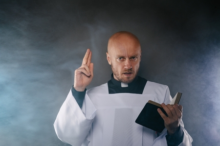 Catholic priest in white surplice and black shirt with cleric collar reading bible and preaching a sermonの写真素材