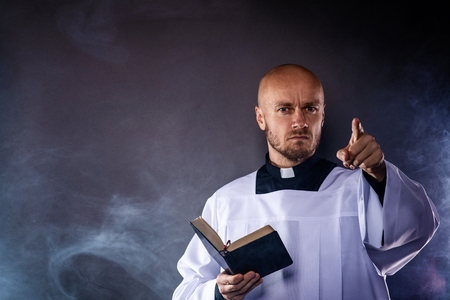 Catholic priest in white surplice and black shirt with cleric collar reading bible and preaching a sermonの写真素材