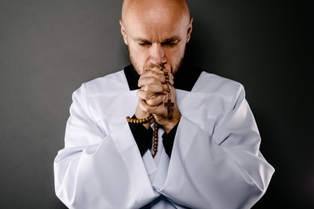 Catholic priest in white surplice and black shirt praying with wooden rosaryの写真素材