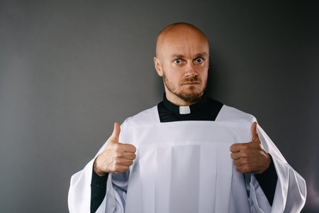 Catholic priest in white surplice and black shirt with cleric collar showing OK signの写真素材