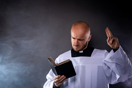 Catholic priest in white surplice and black shirt with cleric collar reading bible and preaching a sermonの写真素材