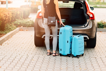 Woman loading two blue plastic suitcases to car trunk. Preparation for tripの写真素材