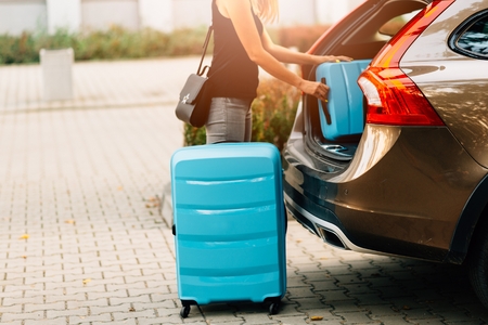 Woman loading two blue plastic suitcases to car trunk. Preparation for tripの写真素材