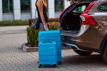 Woman putting two blue plastic suitcases to car trunk. Preparation for tripの写真素材
