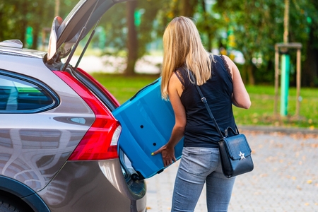 Woman loading two blue plastic suitcases to car trunk. Preparation for tripの写真素材