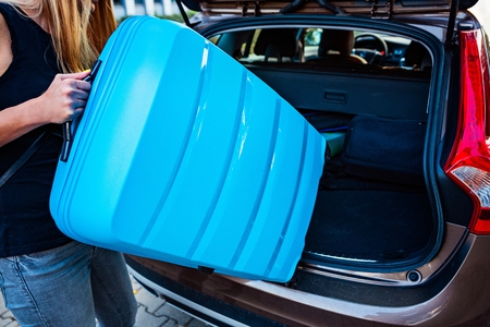 Woman loading two blue plastic suitcases to car trunk. Preparation for tripの写真素材