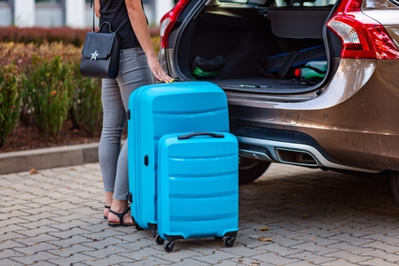 Woman putting two blue plastic suitcases to car trunk. Preparation for tripの写真素材