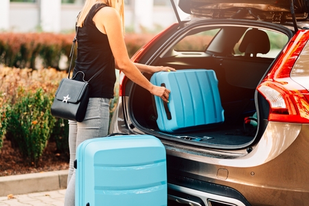 Woman loading two blue plastic suitcases to car trunk. Preparation for tripの写真素材