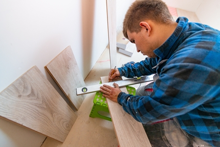 Man measuring and marking laminate floor tile for cutting, installing laminate flooring. Home improvement and renovation conceptの写真素材