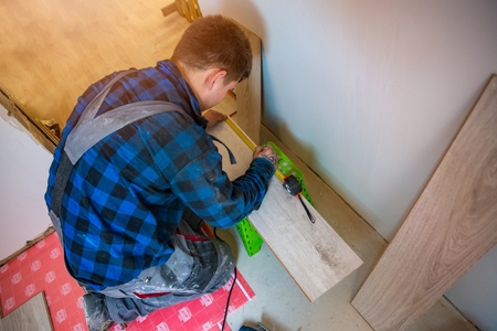Worker measuring and marking laminate floor tile for cutting, installing laminate flooring. Home improvement and renovation conceptの写真素材