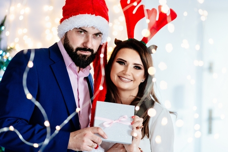 Happy couple in Christmas hats holding gift box. Man and woman at christmasの写真素材