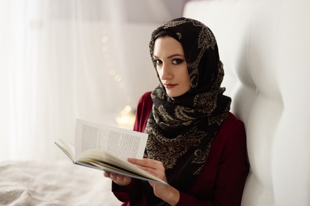 Arabic woman in hijab reading a book in bedroomの写真素材