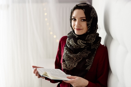 Arabic woman in hijab reading a book in bedroomの写真素材