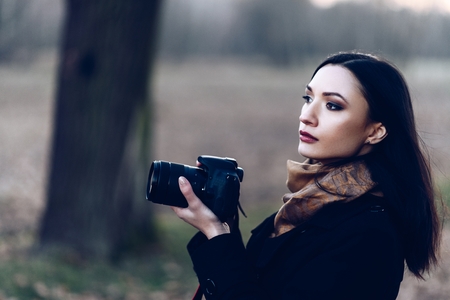 Young brunette woman taking photos with dslr photo camera outdoors