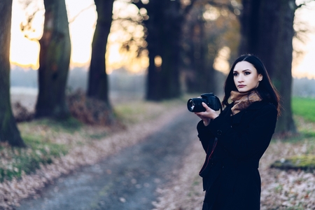 Young brunette woman taking photos with dslr photo camera outdoorsの写真素材