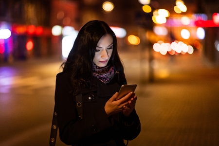 Young brunette woman using mobile phone at night. Smartphone at nightの写真素材