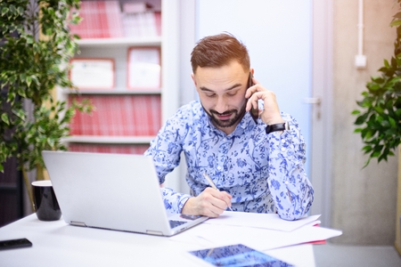 Businessman working on laptop and making a phone call in his office. Man working in officeの写真素材