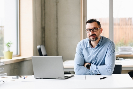 Middle aged handsome man in shirt working on laptop computer in office. Man working in officeの写真素材