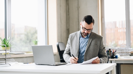 Middle aged handsome businessman in shirt working on laptop computer in office. Man working in officeの写真素材