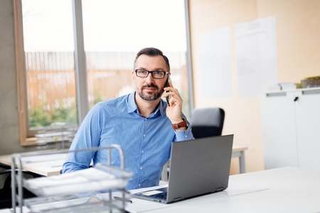 Middle aged handsome man in shirt working on laptop computer in office. Man working in officeの写真素材