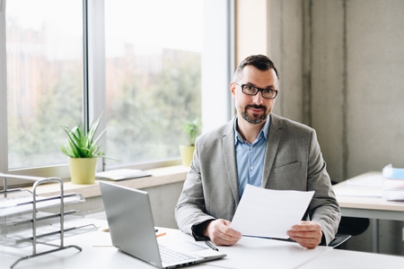 Happy middle aged handsome businessman in shirt working on laptop computer in office. Man working in officeの写真素材