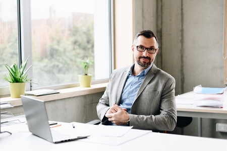 Happy middle aged handsome businessman in shirt working on laptop computer in office. Man working in officeの写真素材